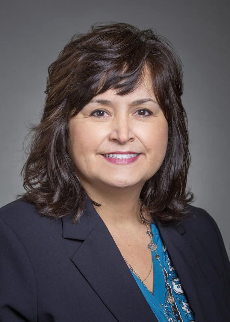 Woman wearing a dark jacket and a blue floral shirt smiling