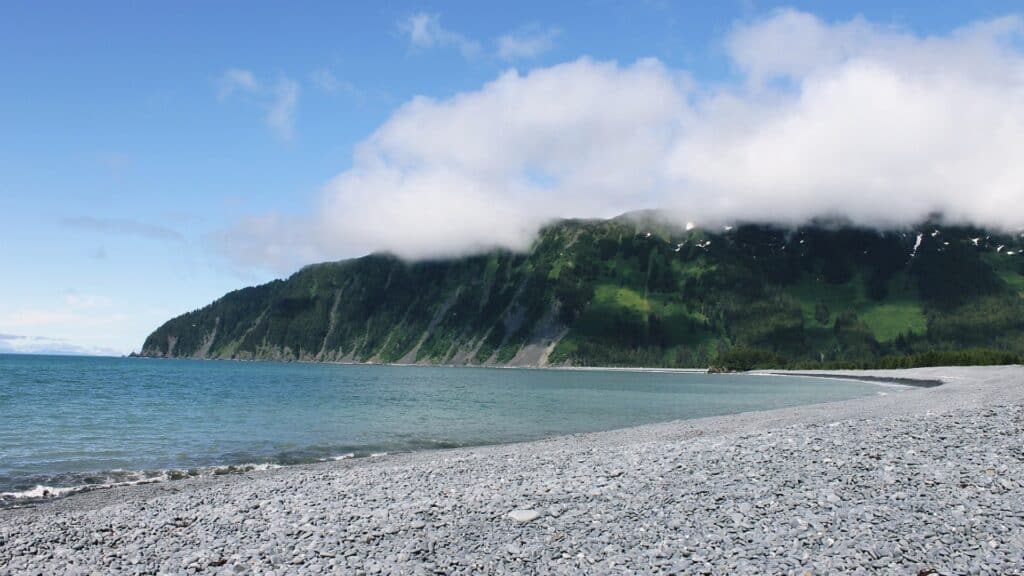 Rocky beach leading towards a steep green mountain